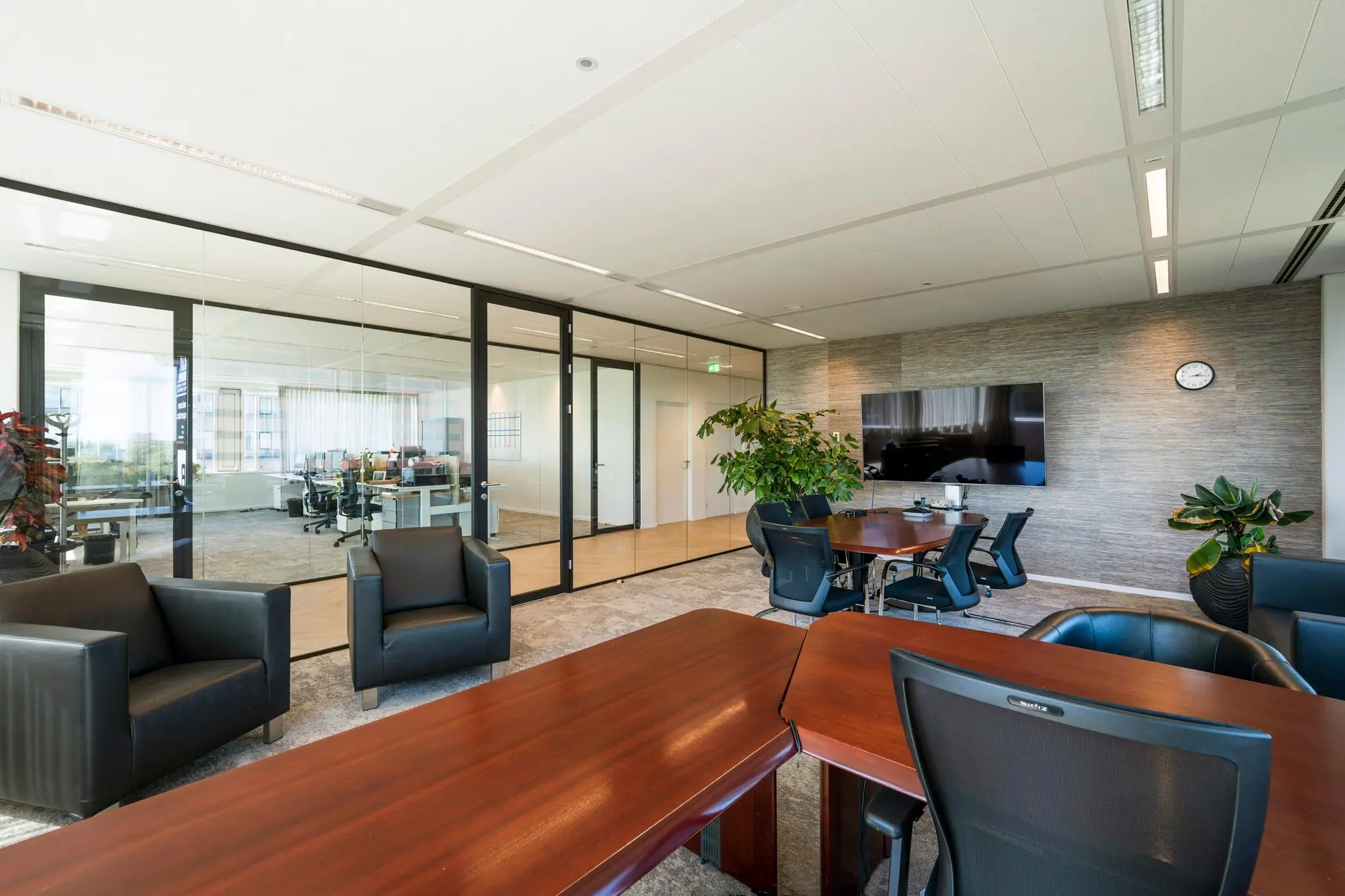 Moderne vergaderruimte aan de Thomas R. Malthusstraat met glazen wanden, lederen stoelen, grote tafel, flatscreen en planten.